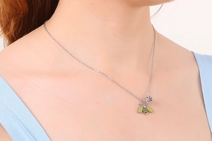Close-up of silver bee necklace with enamel details and flower charm on a female neck