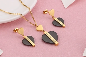 Détail de la parure collier et boucles d'oreilles cœur noir plaqué or sur fond rose