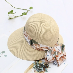 Detail of hand-woven beige straw hat with a floral silk ribbon bow and wide sunshade brim