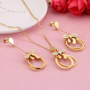 Golden bow jewelry set with oval pendants and white diamonds on pink background
