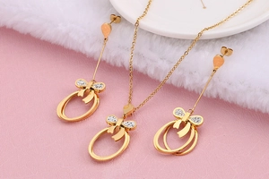 Golden bow necklace and earrings set with white rhinestones on soft pink texture