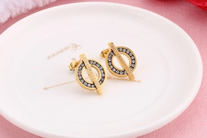Detailed close-up of gold stud earrings featuring sparkling rhinestones and Roman numerals