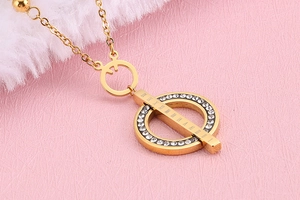 Detailed close-up of a gold necklace featuring a diamond-set ring and Roman numeral bar
