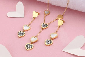 Close-up of golden heart necklace and shell earrings with rhinestones on pink background