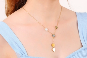 Close-up of a gold Y-shaped necklace with heart-shaped shell and rhinestone pendants