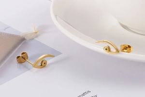 Detailed macro view of golden stylized bird eye stud earrings with metallic finish