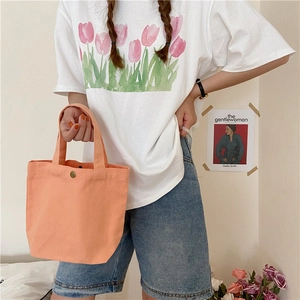 Orange canvas lunch tote bag handheld by woman for casual daily lifestyle