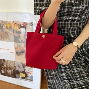 Close-up of red canvas lunch bag showing a golden metal snap button closure and sturdy handles