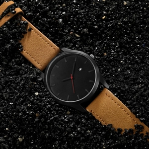 Minimalist quartz men's watch with brown leather strap and black dial on dark rocks