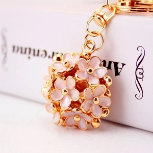 Macro shot of 3D spherical daisy floral keychain in golden metal and soft pink enamel