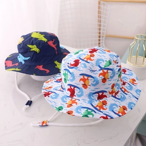 Kids sun hats featuring colorful dinosaur prints and adjustable chin straps on a marble table