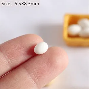 Detailed view of miniature 5.5x8.3mm white dollhouse eggs on a fingertip for scale