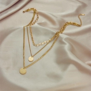Layered gold titanium necklace with engraved circular pendants on beige silk background