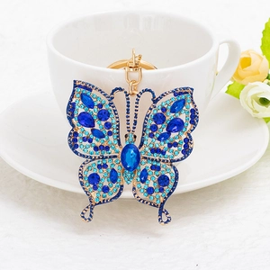Blue butterfly rhinestone keychain with gold lobster clasp on a white coffee cup