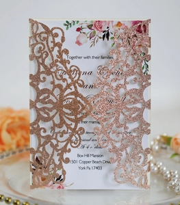 Close-up of laser-cut rose gold glitter wedding invitation with floral insert and pearls