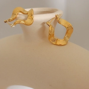 Irregular wave-patterned gold-plated titanium steel earrings displayed on a ceramic vase
