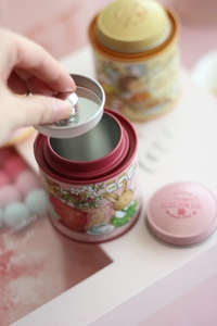 Detailed view of pink and yellow tin storage canisters with double-lid sealing design