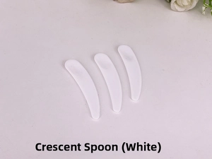 Close-up of three white crescent-shaped plastic cosmetic spatulas for facial cream