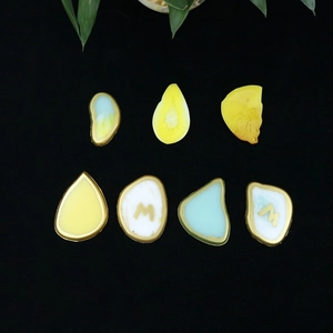 Detail of seven irregular resin charms in yellow, blue and white with gold edges