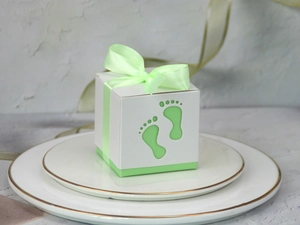 Detail of baby footprint cutout on light green gift box with a satin ribbon on marble tiles