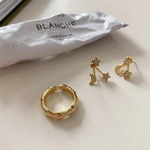 Close-up of golden bamboo texture ring and celestial earrings on minimalist background