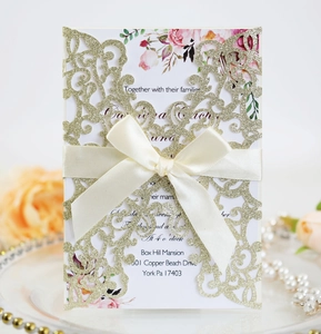 Detail of laser-cut glitter gold wedding invitation with floral card and beige ribbon