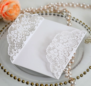 Detail of white laser-cut floral wedding invitation card with elegant pearl decoration