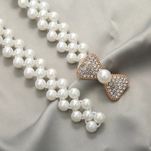 Close-up of pearl waist chain with a sparkling gold bow buckle on grey silk fabric