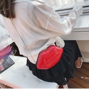 Detailed view of a red lip-shaped crossbody bag with gold chain strap on a model