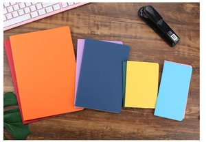 Colorful A5 B5 notebook assortment on desk with pink keyboard and office supplies