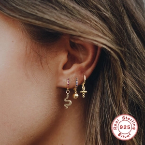 Set of 925 sterling silver gold earrings with snake, bead and cross charms on a model