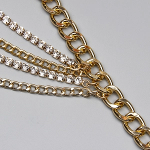 Détail de chaînes dorées multicouches et de bandes de strass brillants sur fond gris