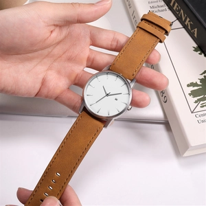 Detail of minimalist quartz watch with white dial and light brown leather strap worn by a person