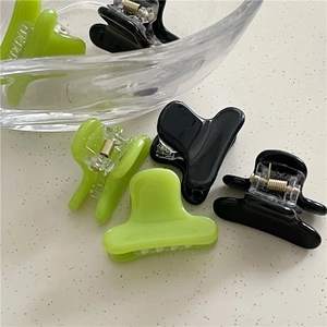 Mini acetate hair claws in green and black colors on a minimalist beige background
