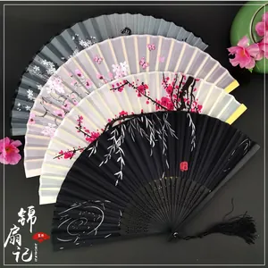 Detailed view of Chinese folding fans with floral patterns and silk tassels on black background