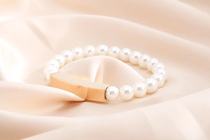 Detailed macro view of white pearl bracelet with rose gold metal plate on silk fabric