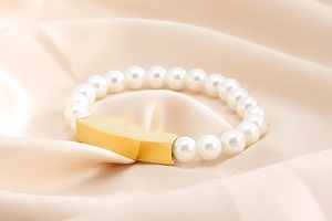 Macro shot of pearl bracelet with golden polished rectangular bar on silk background