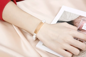 Detailed view of elegant white pearl bracelet with gold-tone metal plate on silk fabric