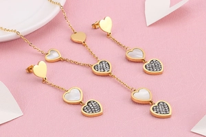 Elegant gold heart jewelry set with white shell and crystals on pink texture