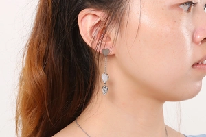 Detail of silver heart tassel earrings with sparkling white shell insets on a model