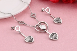 Parure de bijoux cœur en argent avec collier et boucles sur fond rose texturé