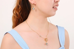 Gros plan sur l'ensemble collier et boucles d'oreilles cœur dorés porté par un mannequin
