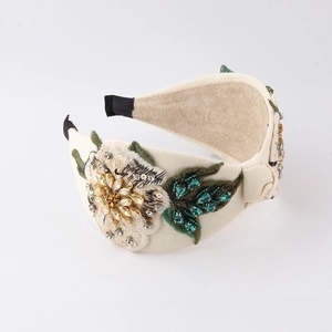 Macro shot of 3D white flower embroidery and emerald rhinestones on a wide headband
