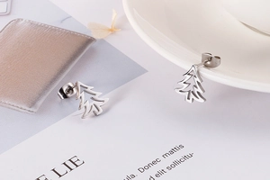 Detailed close-up of silver hollow Christmas tree stud earrings on a white display card