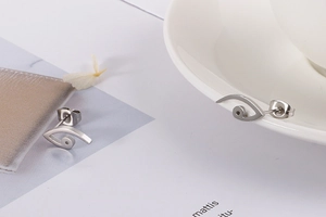 Detailed close-up of geometric eye earrings in silver-tone stainless steel on a white cup