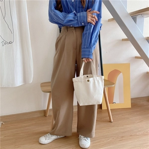 Close-up of cream canvas mini tote bag with metal buckle held by model in home setting