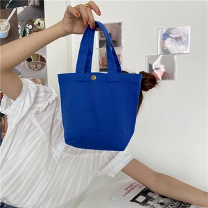 Close-up of bright blue canvas lunch bag with a gold snap button held by a model