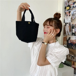 Close-up of a small black canvas lunch bag with metal snap button used as a handbag