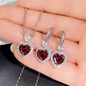 Close-up of heart-shaped necklace and earrings set with red stones held by hand