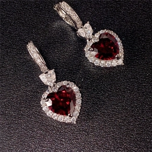 Detailed view of silver heart earrings with dark red gemstone and sparkling clear halo